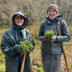 Two girls in raincoats holding weeds and shovels.